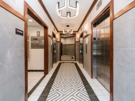 An elevator lobby with gray tiled walls, wood trim, two stainless steel elevators, and a geometric patterned floor.