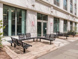 Black metal outdoor benches arranged on a paved patio outside a building entrance.