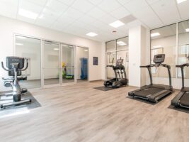 A fitness room with a stationary bike, an elliptical, and treadmills on light wood flooring.