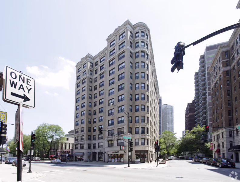 A tall, light-colored stone apartment building on a city street corner with a 7-Eleven on the ground floor.